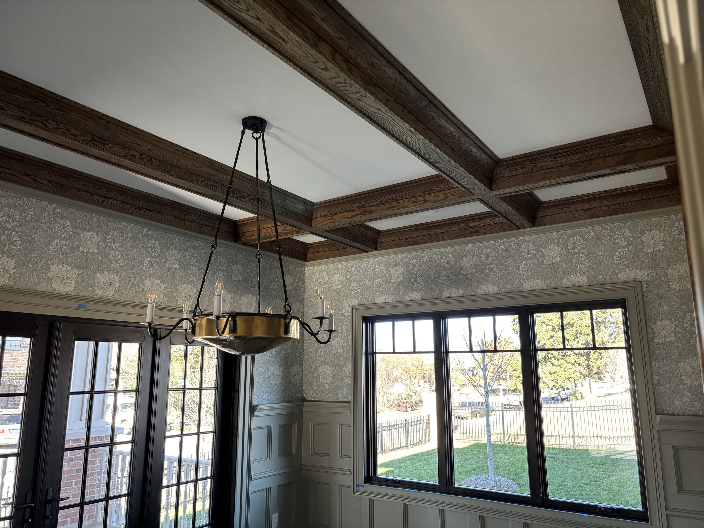 Dining room with exposed oak ceiling beams, brass chandelier, and tapestry wallpaper