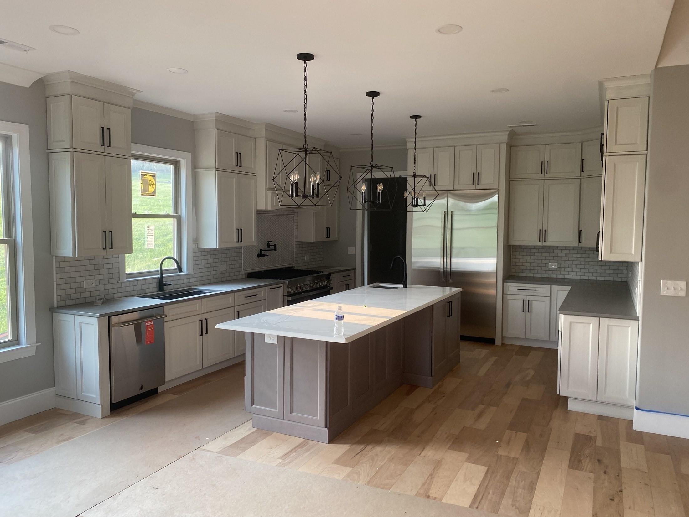 Kitchen with white shaker cabinets, geometric pendants, and wide-plank floors near completion