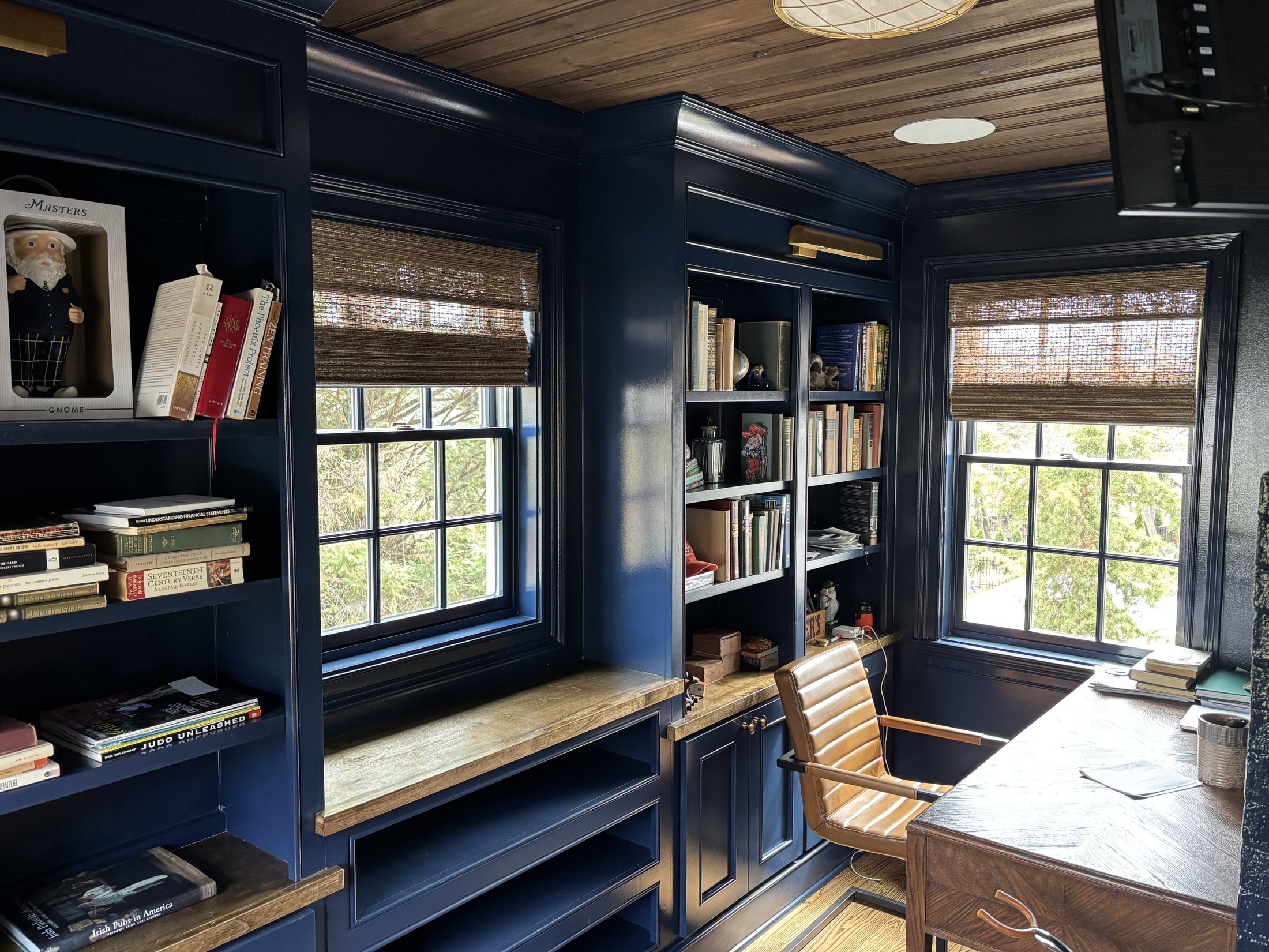 Navy-painted home library with built-in bookcases, window seats, and oak desk